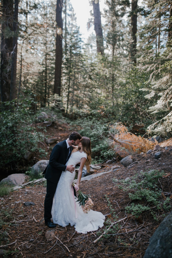 groom kissing bride while dipping her in the middle of the woods by a creek located in the Smoky Mountains Tennessee. Fall boho wedding trend. wooded forest wedding.