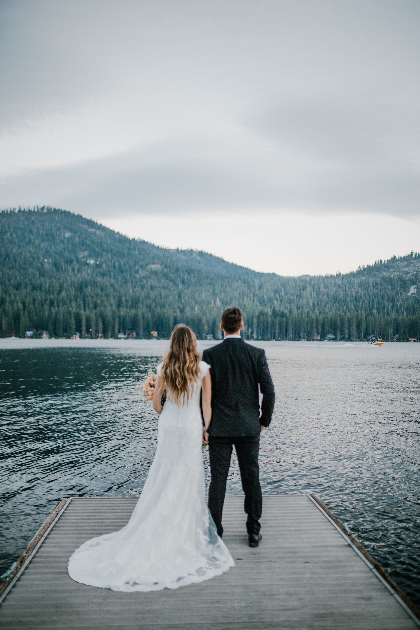 bride and groom standing at the end of a dock in a lake n Knoxville Tennessee looking out into the water and the rolling hills covered in pine trees on their wedding day