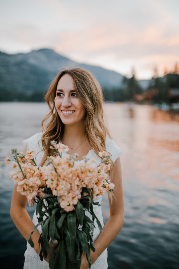 fall bride standing on a lake with the smokies behind her wearing a boho gown with pink bouquet in Tennessee 