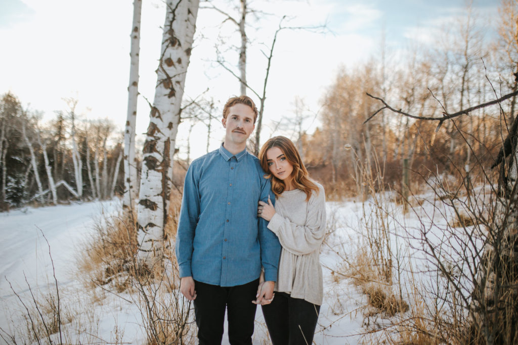 winter engagement session in the smokies, and wearing a blue button down and a mustaches is holding the womans hand as she leans into him