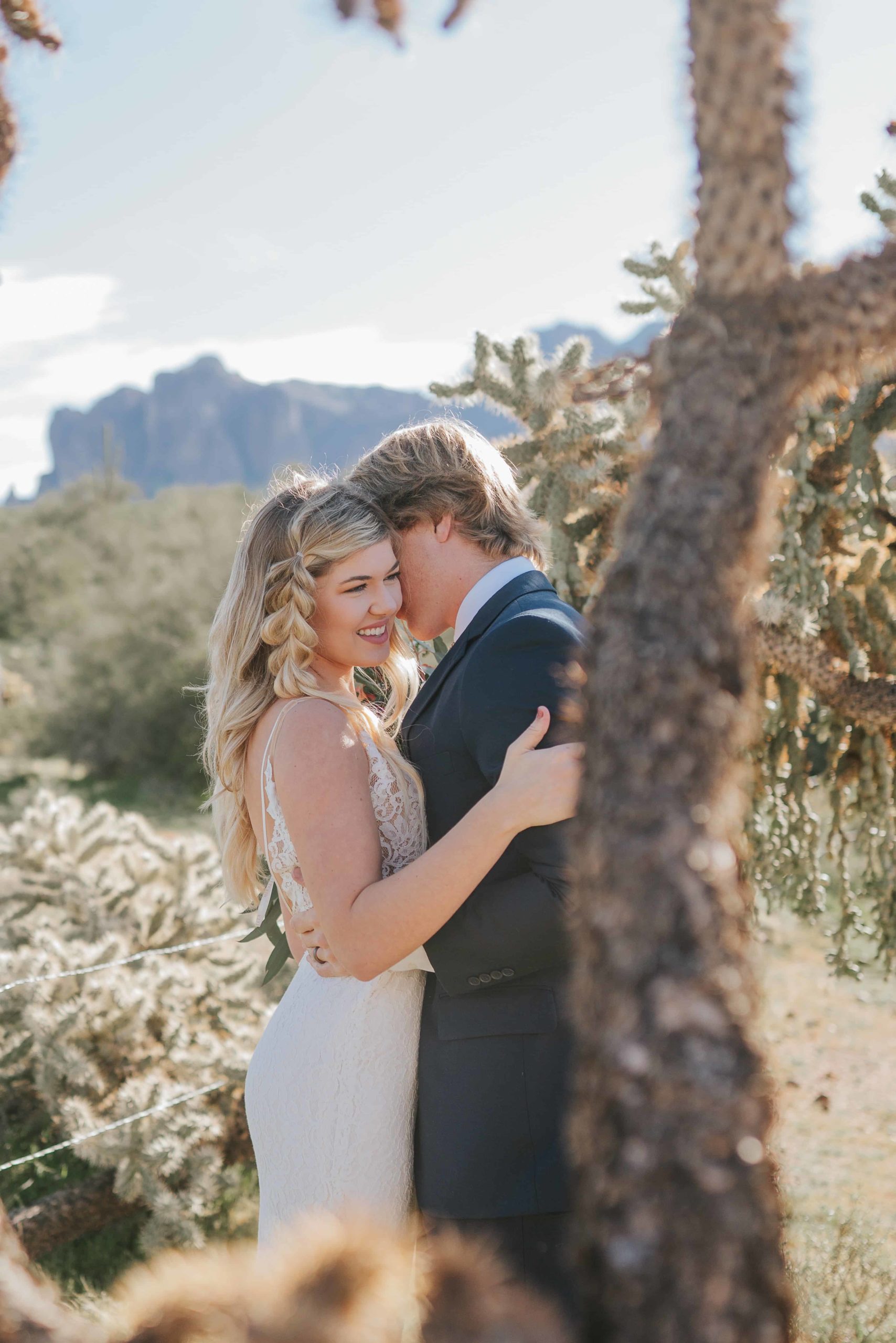 bride and groom hugging and laughing behind a tree in joshua tree budget friendly wedding