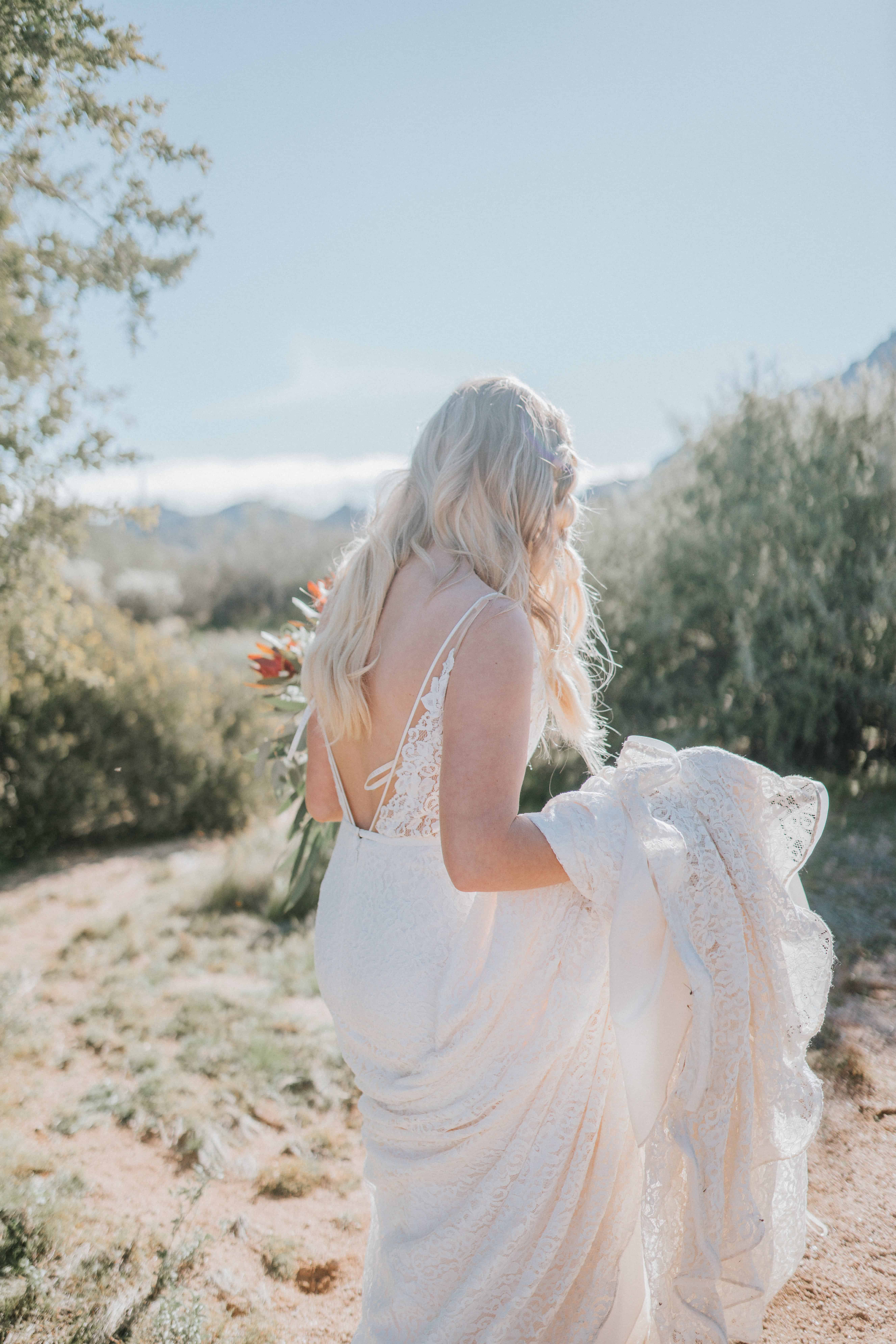 Back shot of bride walking outside while holding the bottom portion of her wedding dress