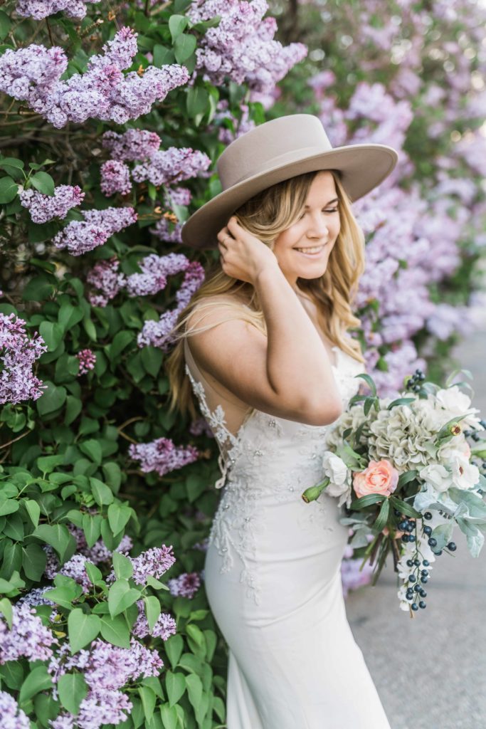 lavender florals with bride wearing a lace gown wearing a hat in boho wedding