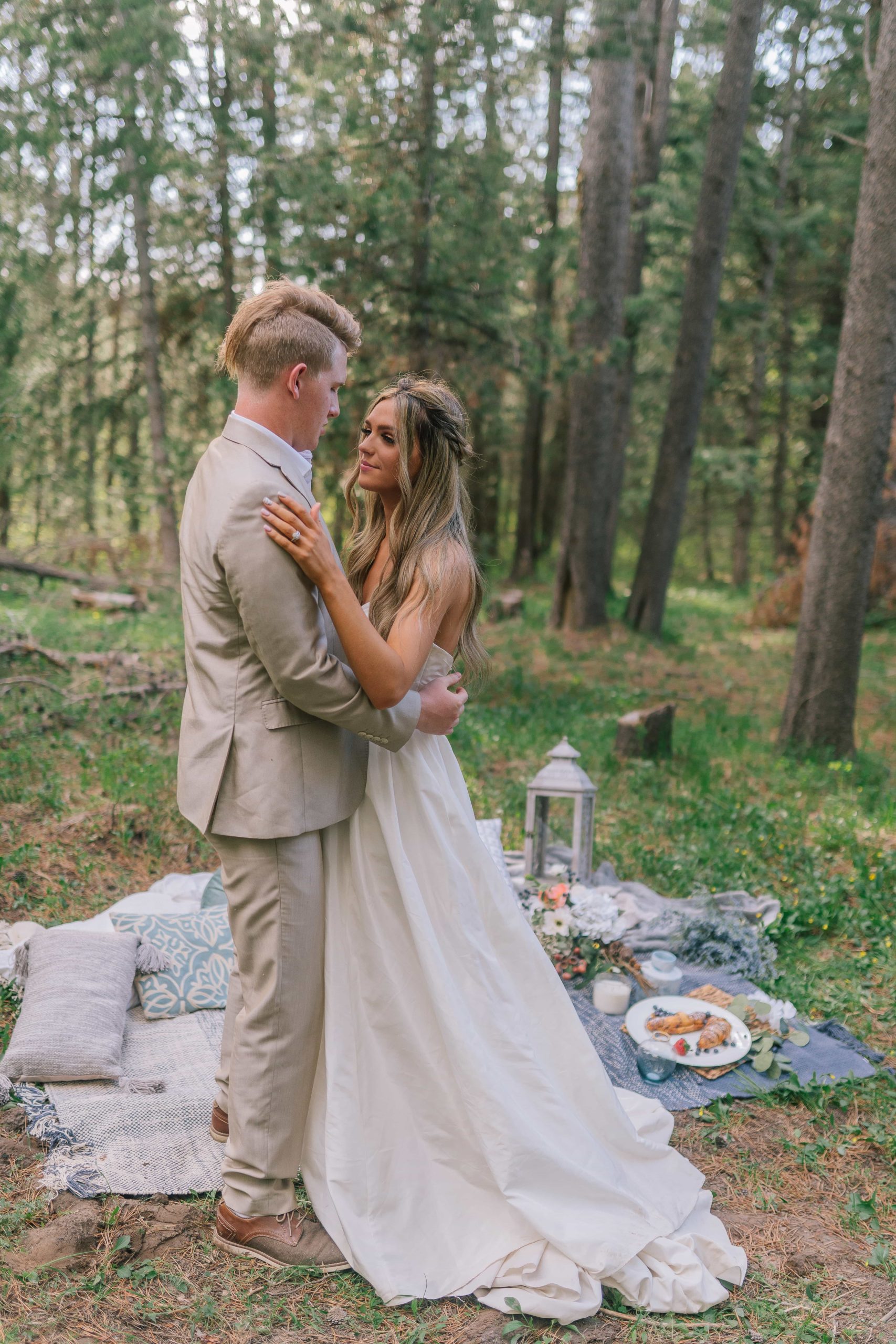 Groom and bride looking at each other while standing on a picnic blanket with pillows