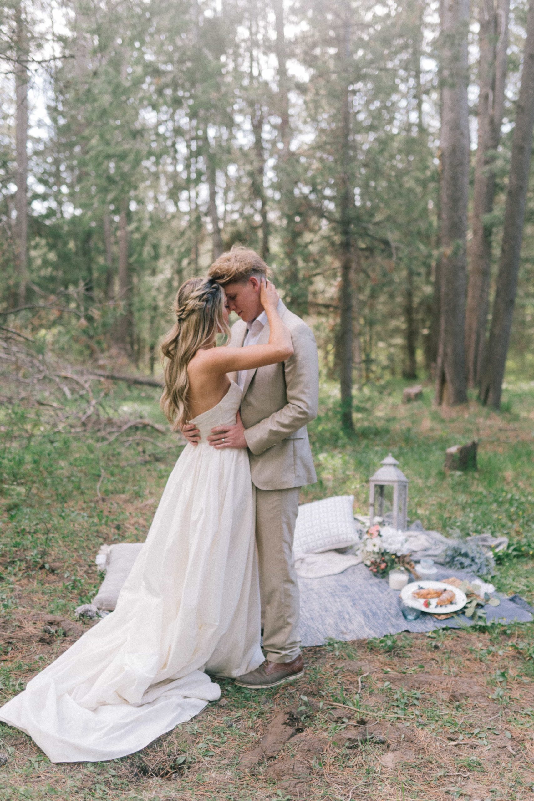 Bride and Groom standing holding each other in front of a picnic in the forest