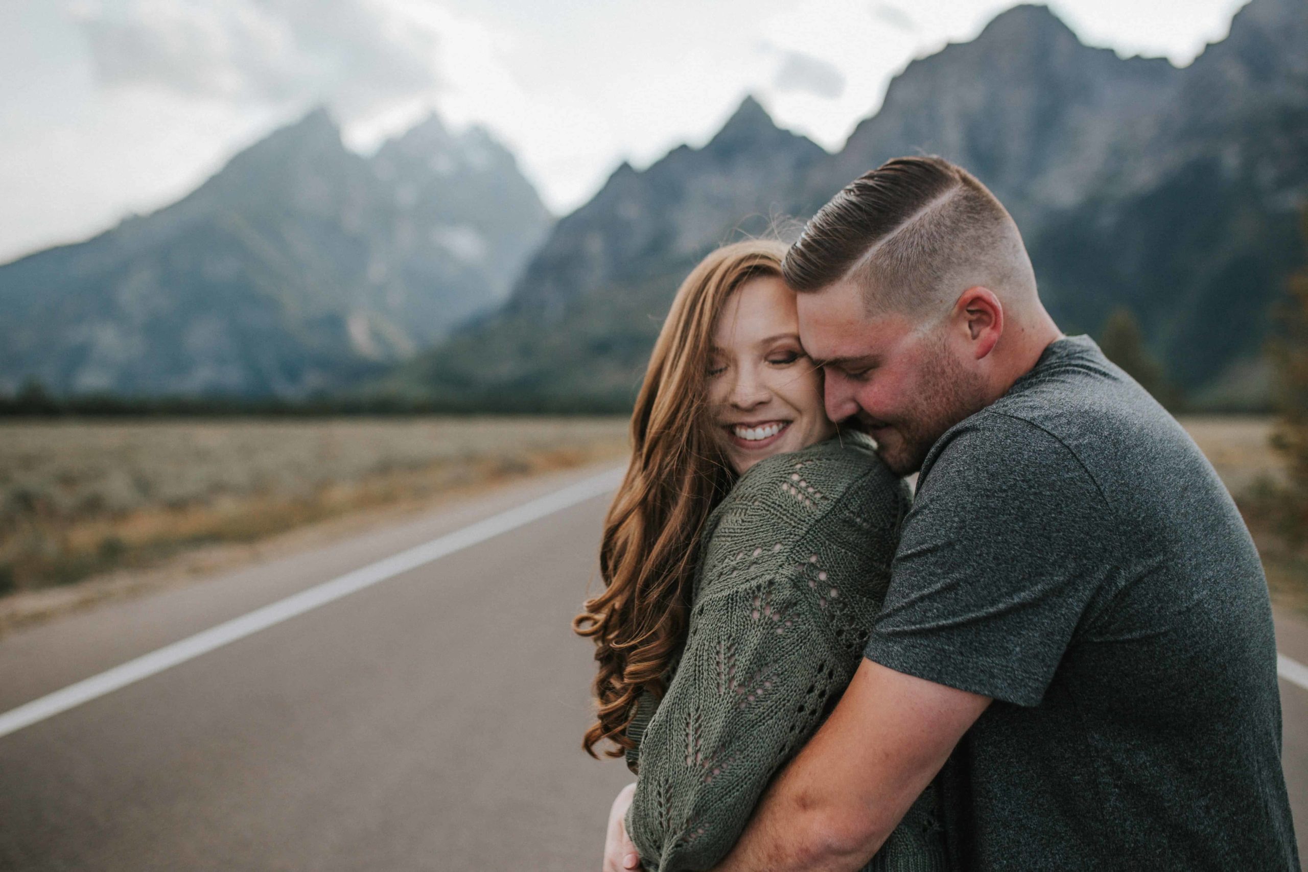 man holding his fiance in front of a mountain range while standing on an open road