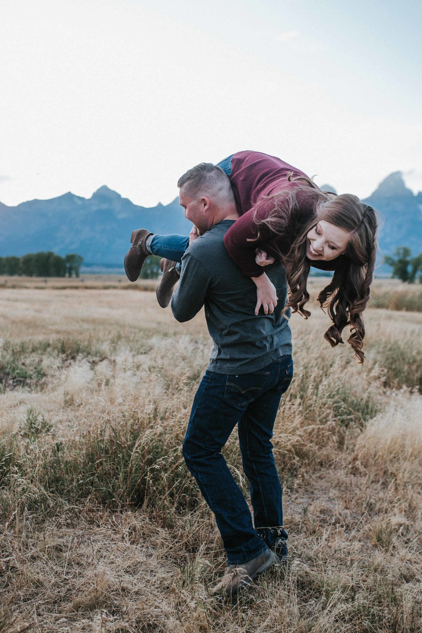 man picking up the woman and carrying her through a field for their fall engagement session