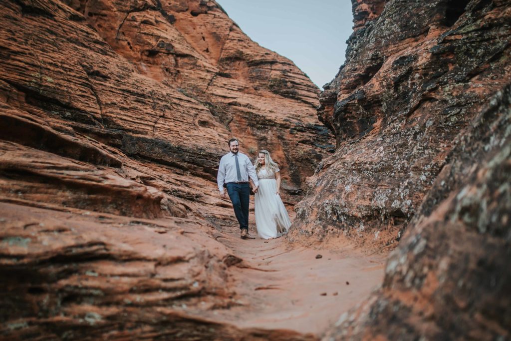 bride and groom walking through a red rock cannon together holding hands in their wedding attire