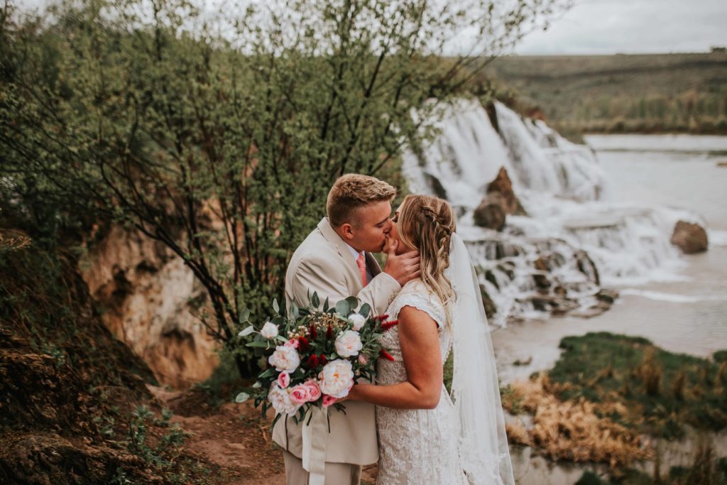 husband and wife kissing in front of the rocky waterfall