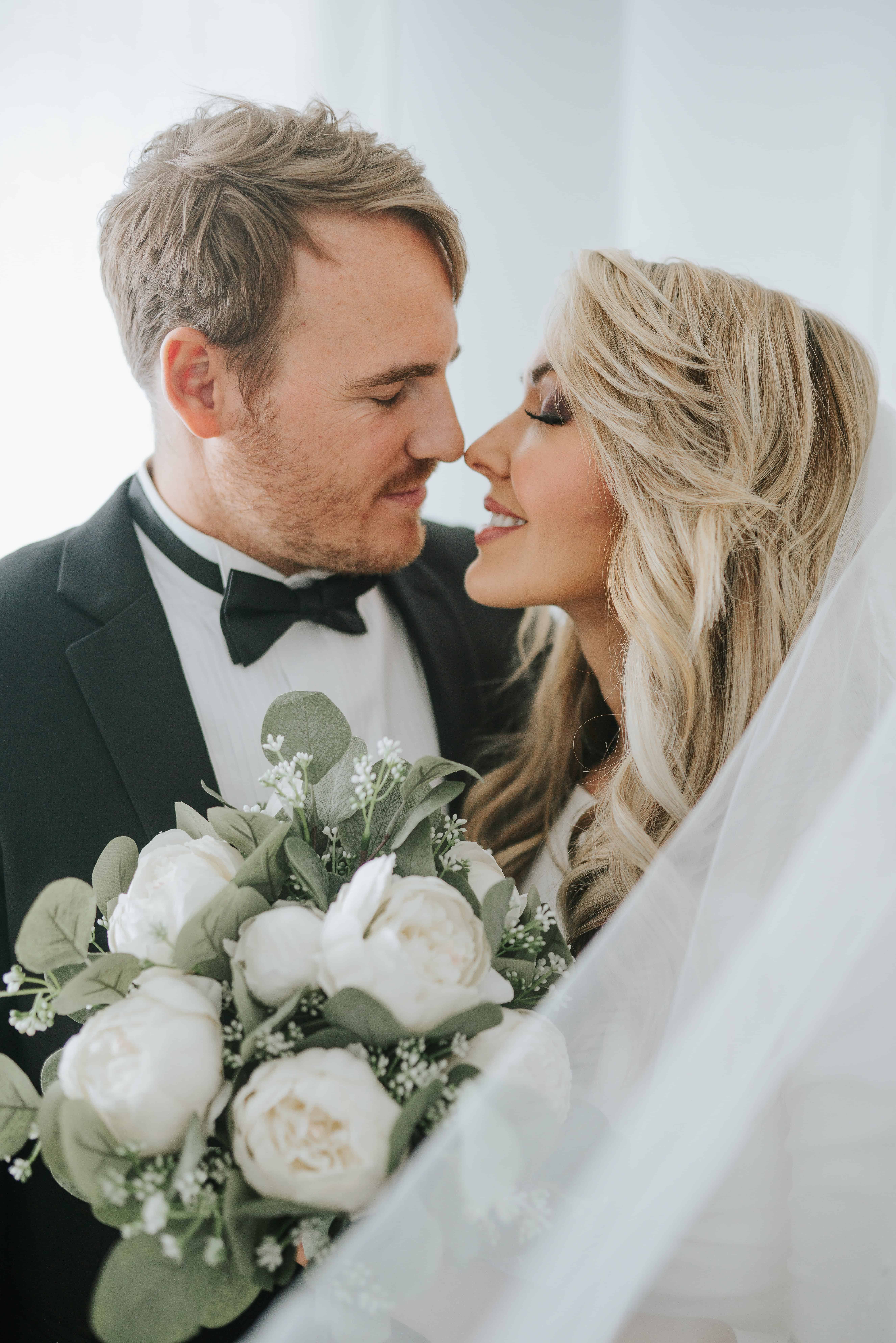 bride and groom leaning into a kiss while holding her floral arrnagement