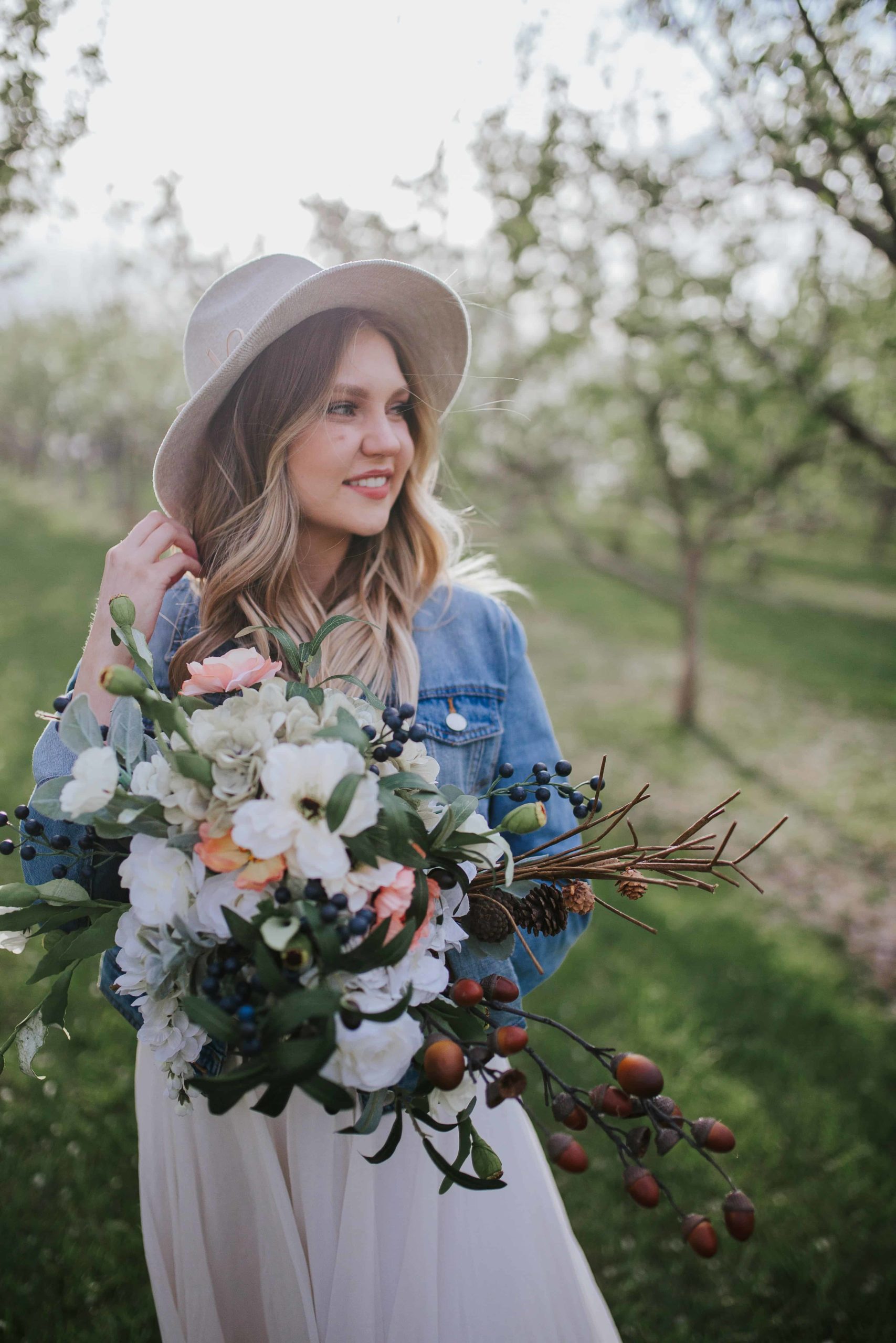 boho chic bride wearing a cream hat and denim jacket with wedding dress holding bouquet