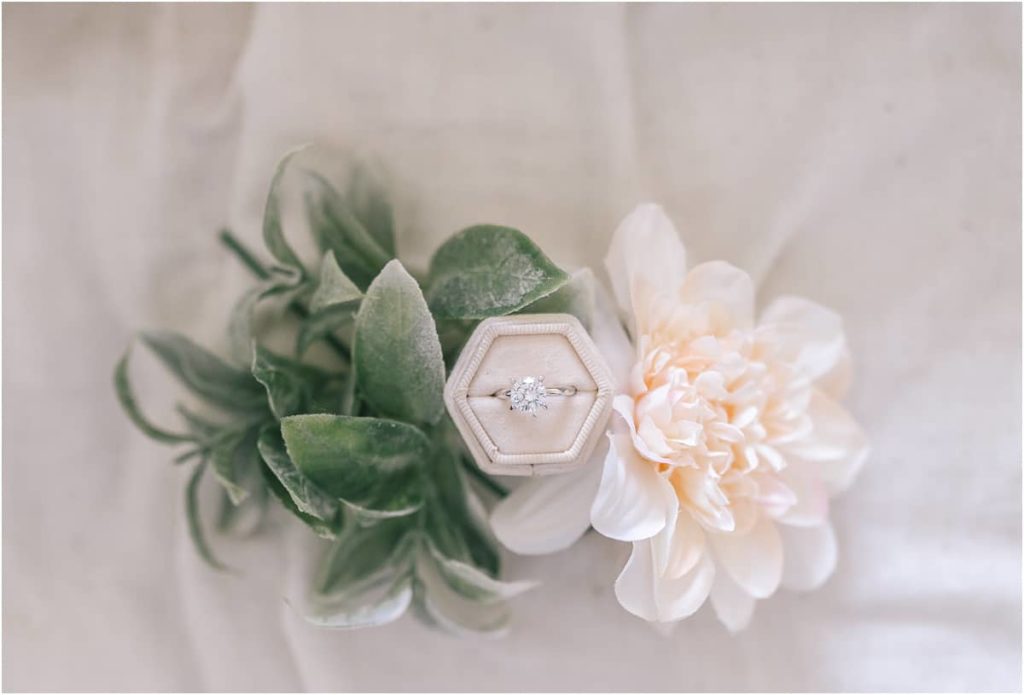 Detail shot of an engagement ring, surrounded by the greenery and flowers used in the wedding.