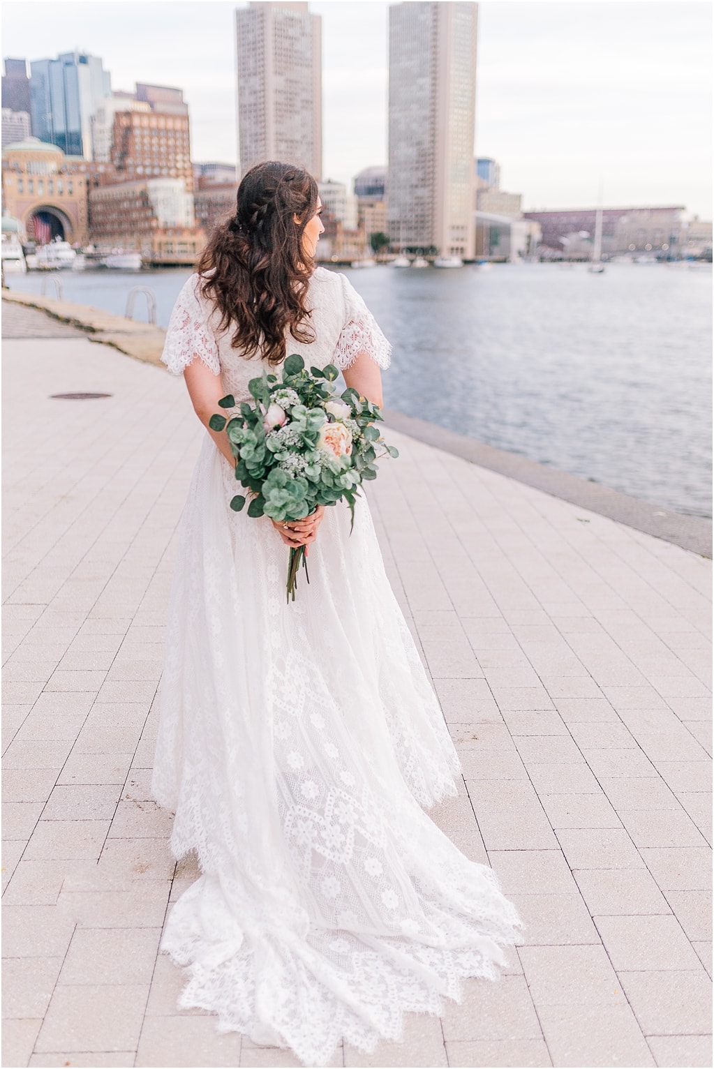 the backside of the bride holding the wedding bouquet behind her while she looks out at the water