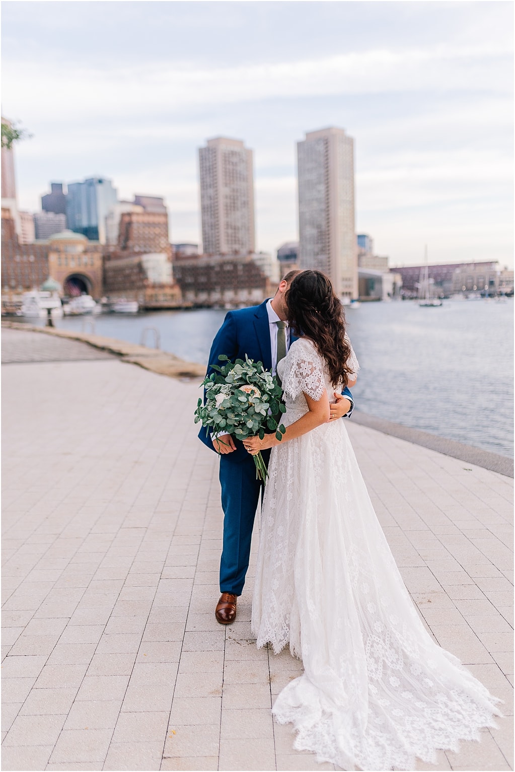 Sacramento wedding photographer captures bride and groom standing on the water with the skyline behind them and kissing on their wedding day