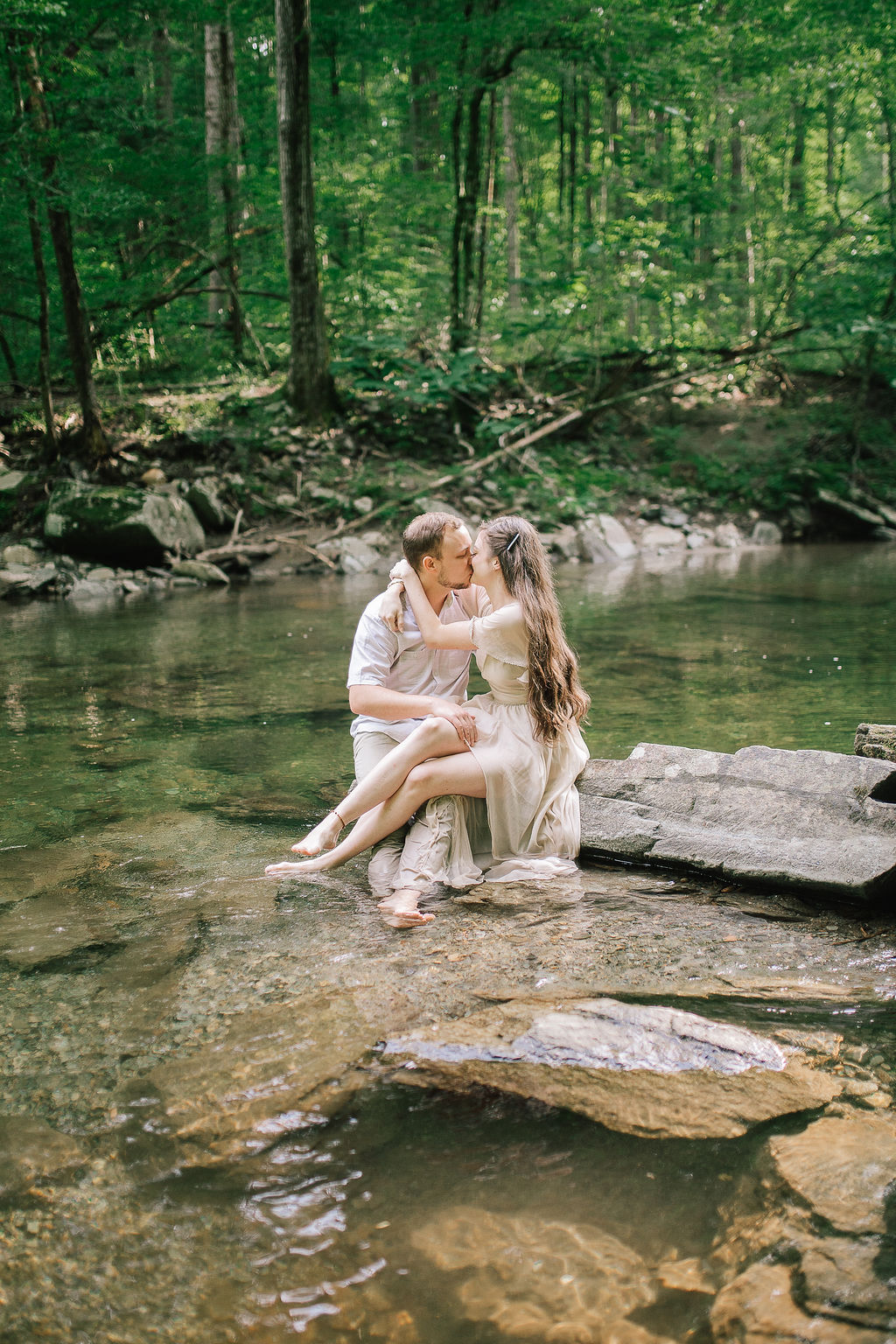 bride sitting with her groom in a babling river in the Smoky Mountains for an enegagement session