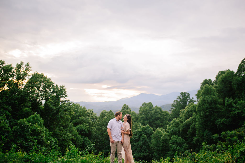bride and groom in the smoky mountains to be married in front of lush trees and a cloudy pink sky holding each other