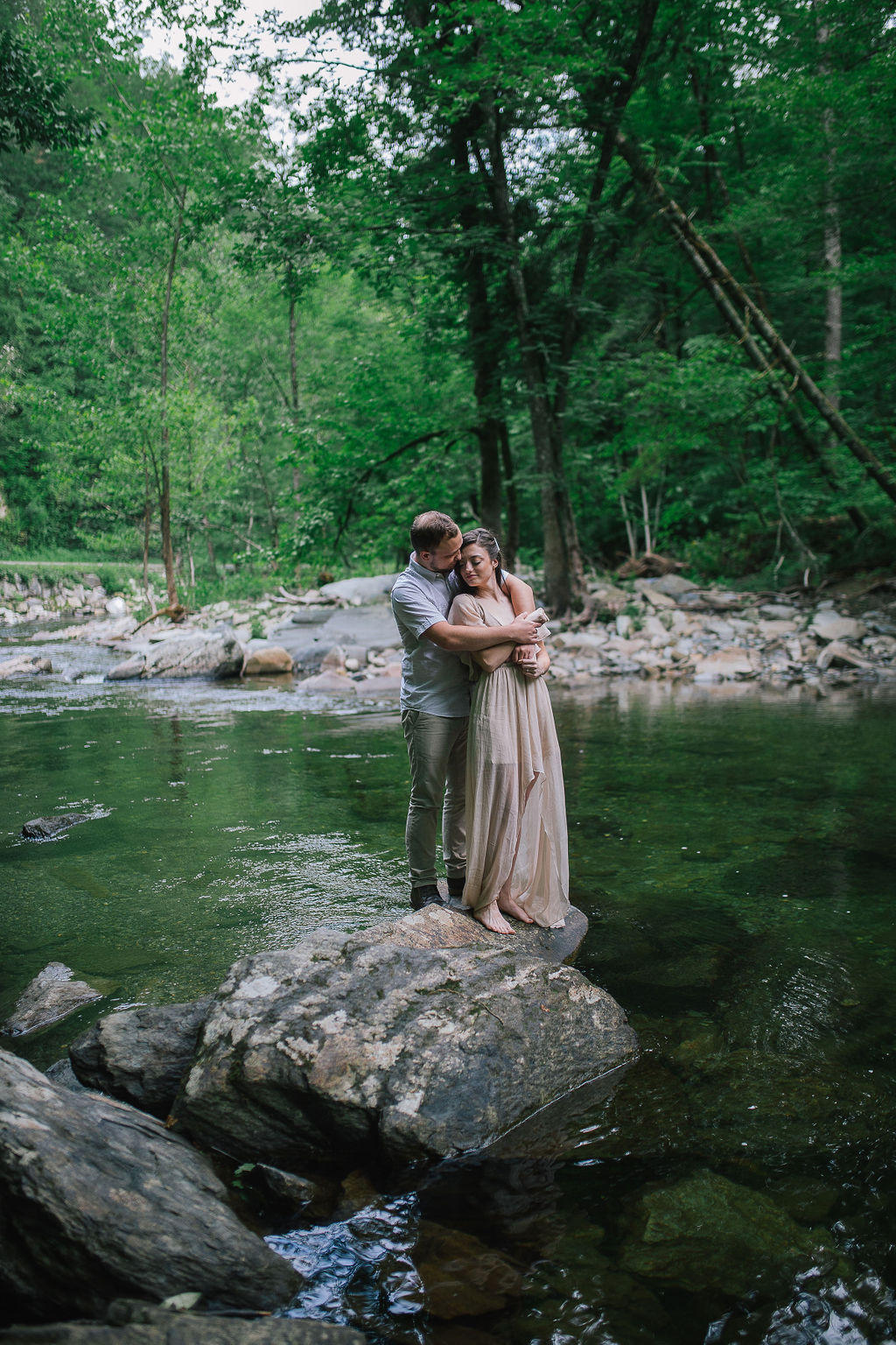 engaged coupple standing in a river in the Smoky Mountains hugging each other