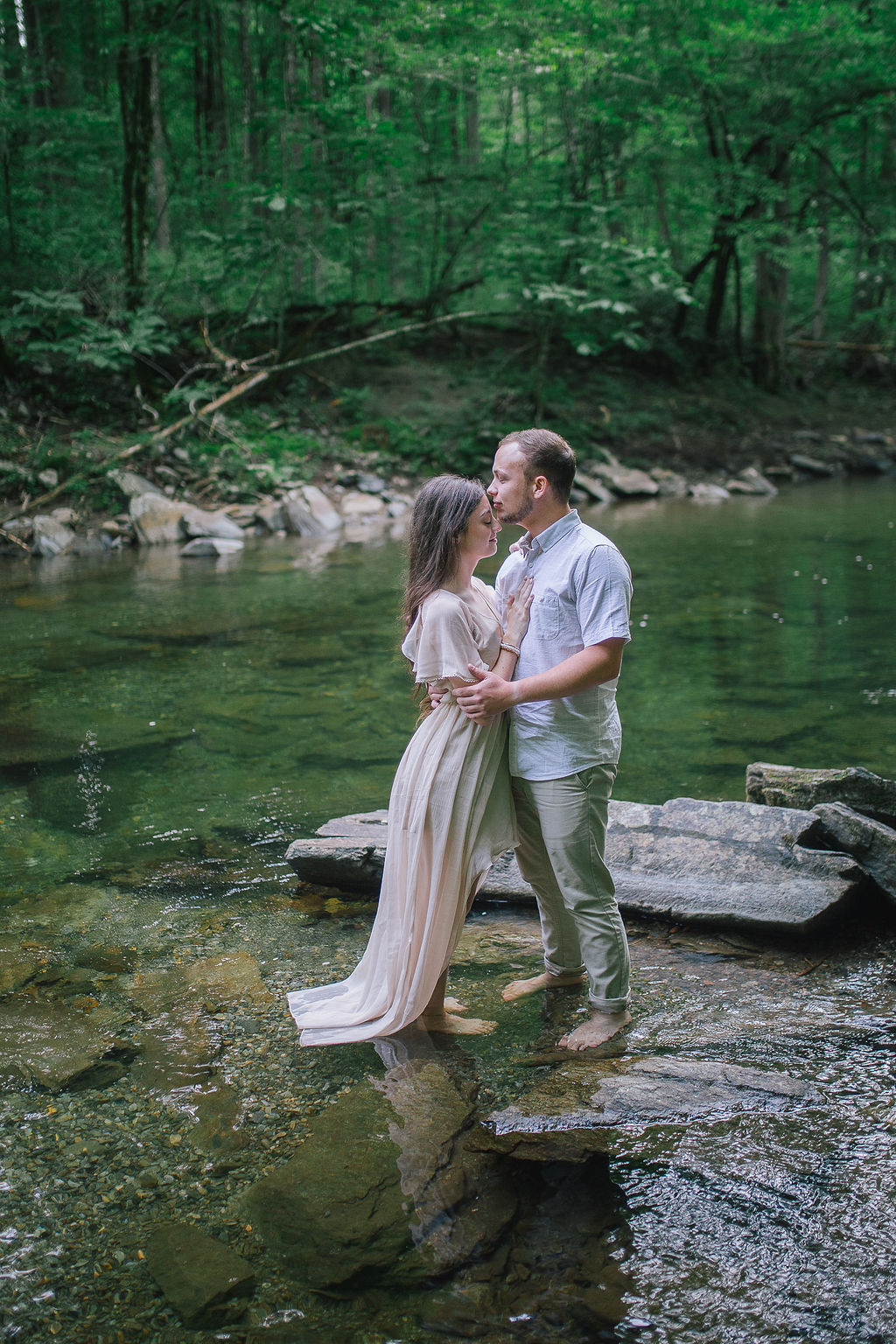 groom kissing his brides forehead while standing in a river in the woods
