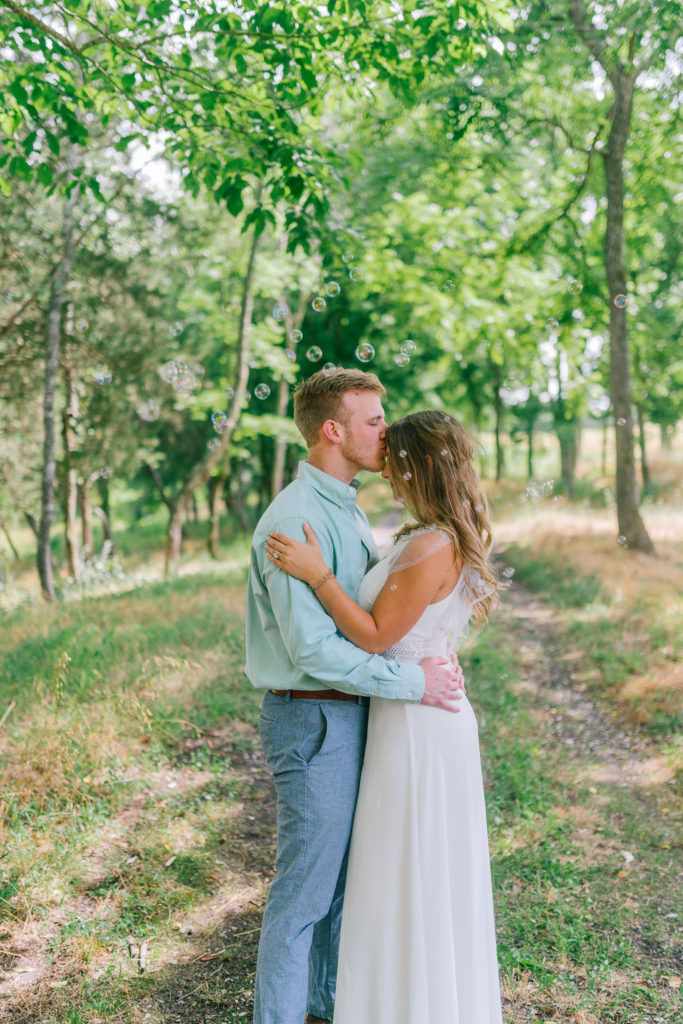 groom ramantically kissing his bride on her forehead in the middle of a wooded area