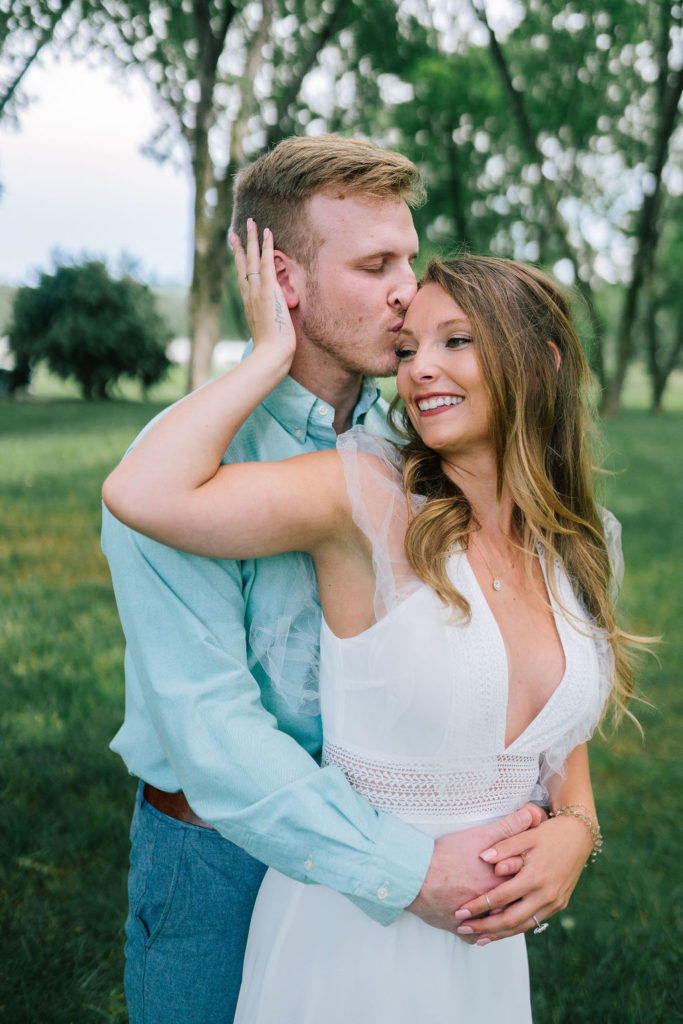 Groom holding his bride from behind and kissing her head. The bride is reaching back to hold his cheek. They are located on Marblegate Farm in Knoxville Tennessee