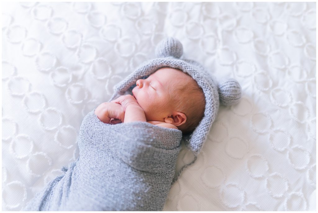 newborn in a grey swaddle on a white sheet