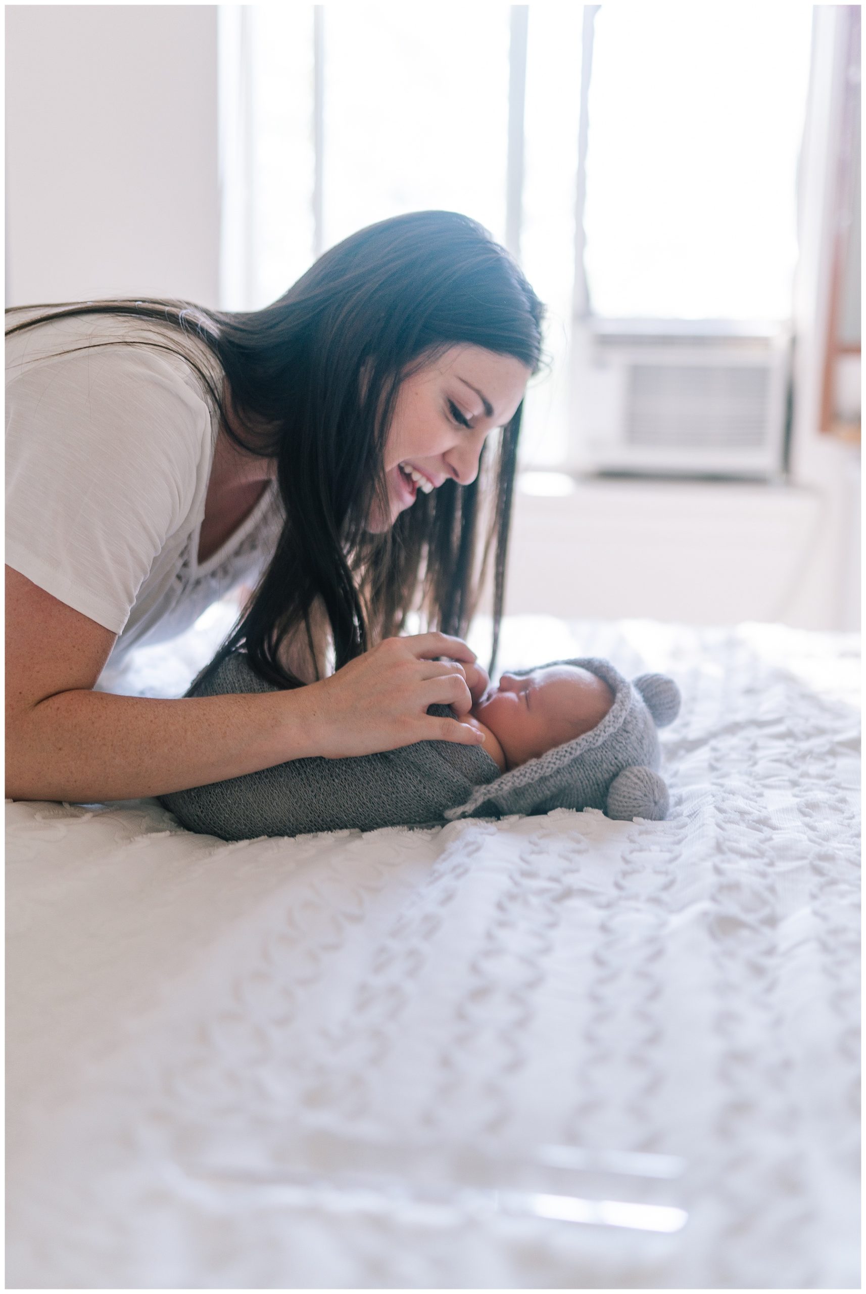 mom wrapping her baby boy in a swaddle in her apartment on a white bed