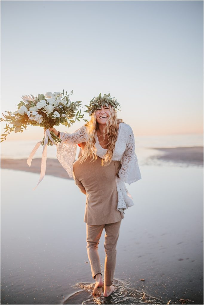 Groom carrying bride over his back while she smiles and holds her bouquet in the Outer Banks