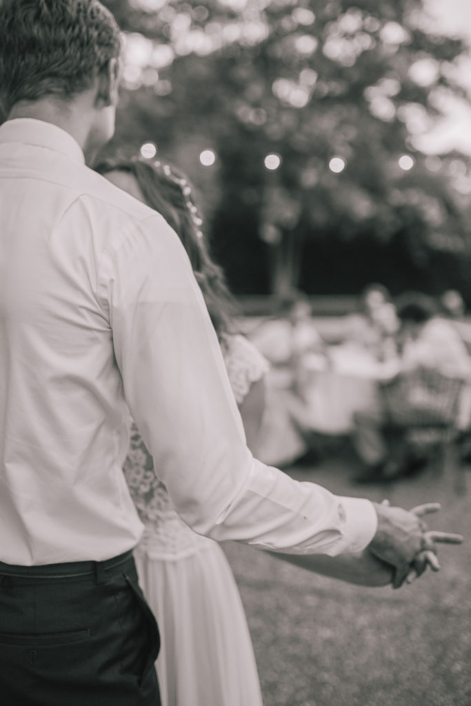 black and white photo of bride and groom holding hands while dancing 