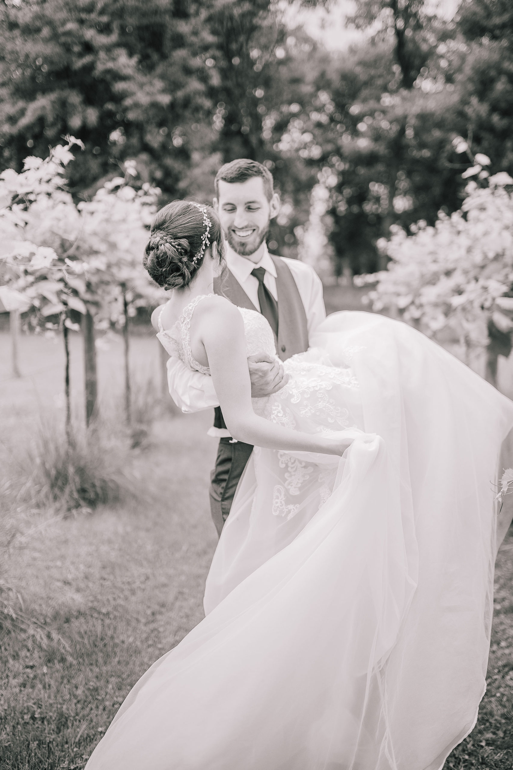 black and white photo of a groom carrying his wife through a vineyard