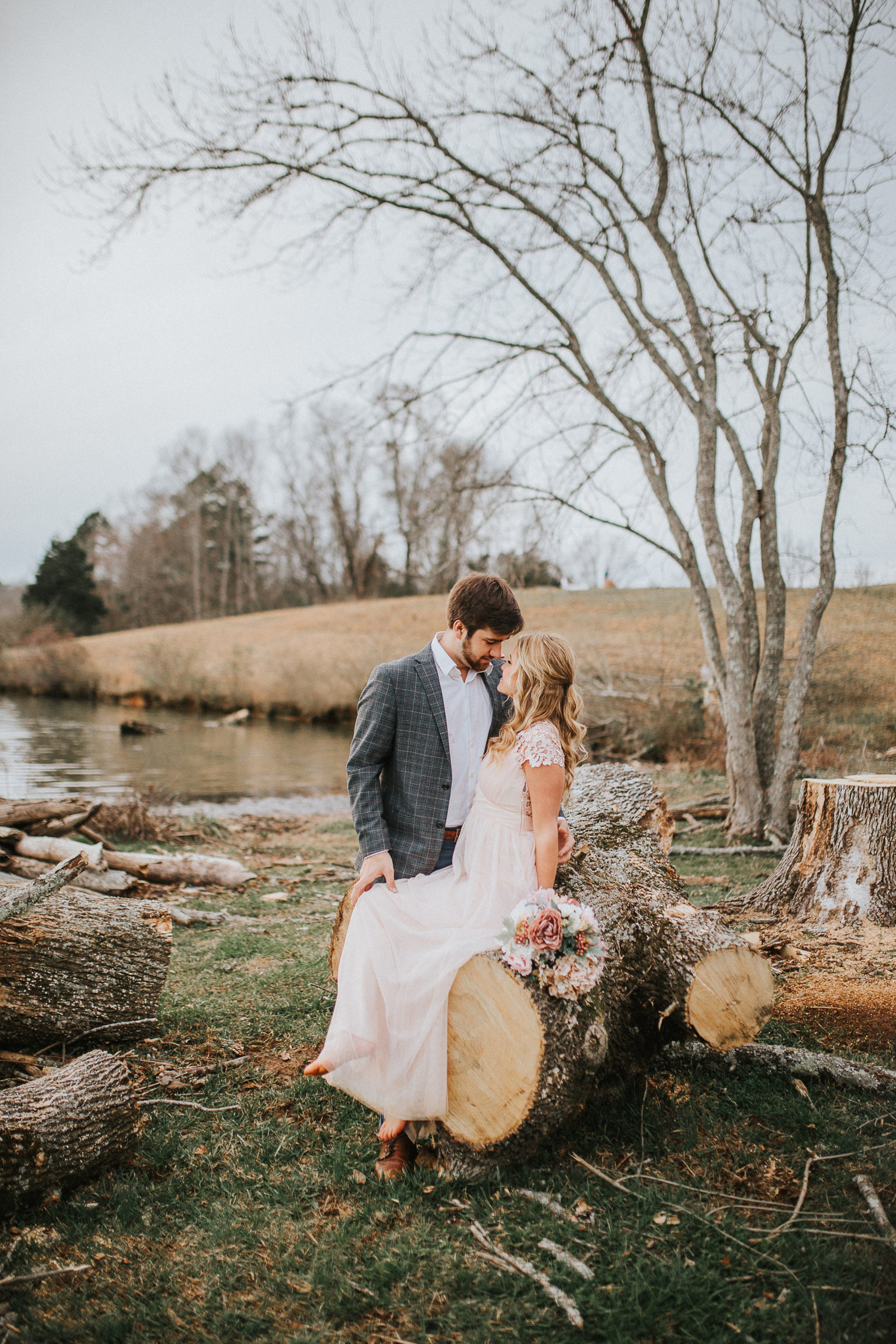 bride sitting on a large log as her groom kisses her head