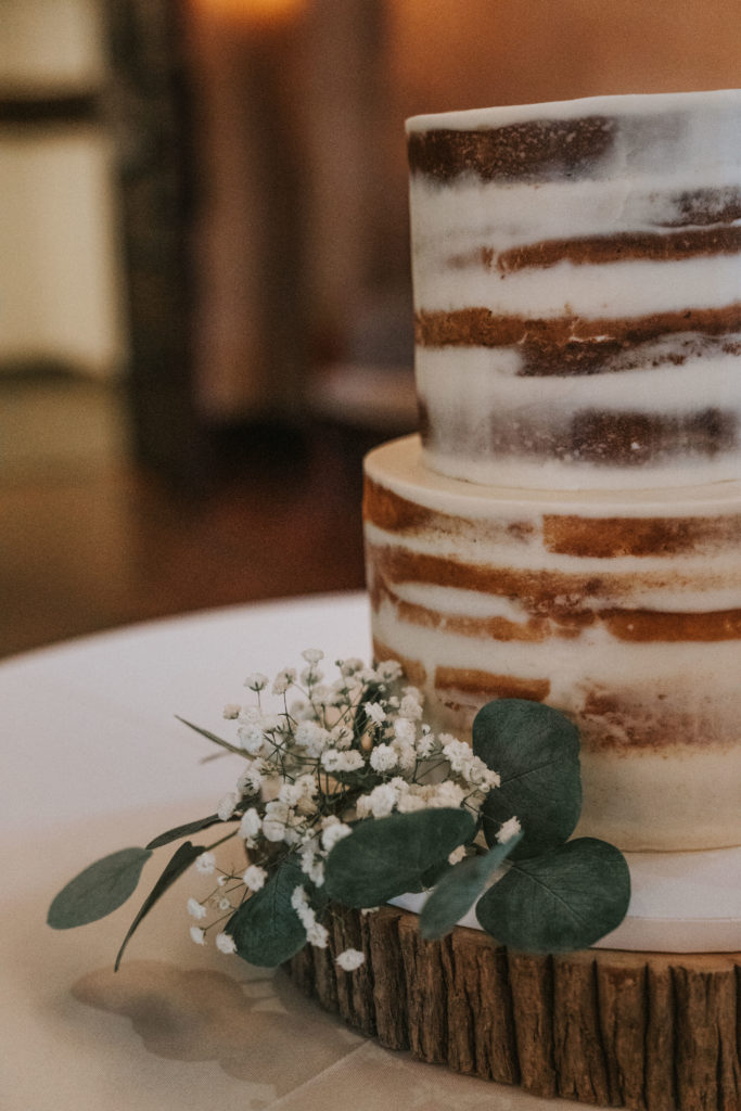 Up close view of a trendy wedding cake, showing the greenery and floral accent.