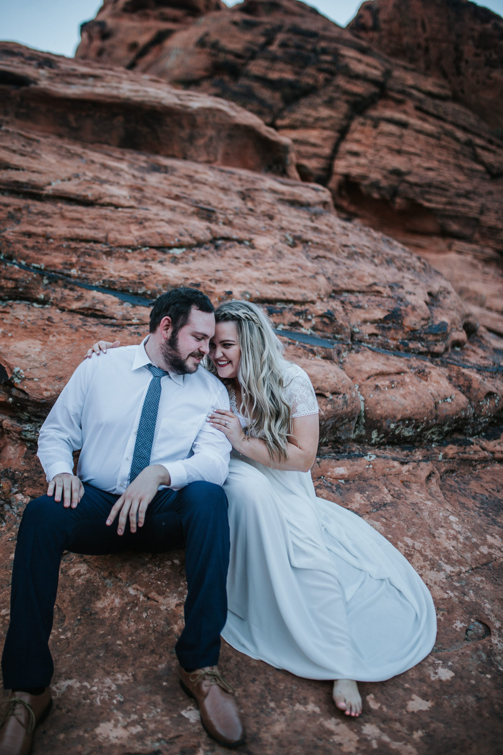 husband and wife on their wedding day sitting on some red rocks in the desert