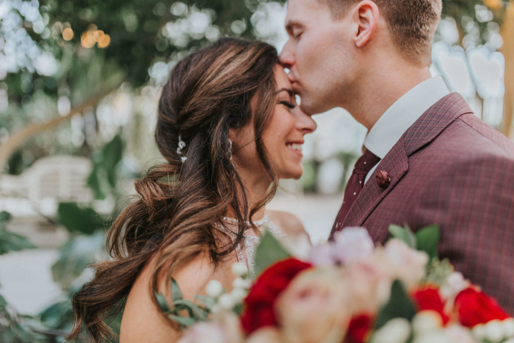 husband kissing his brides forehead as she smiles