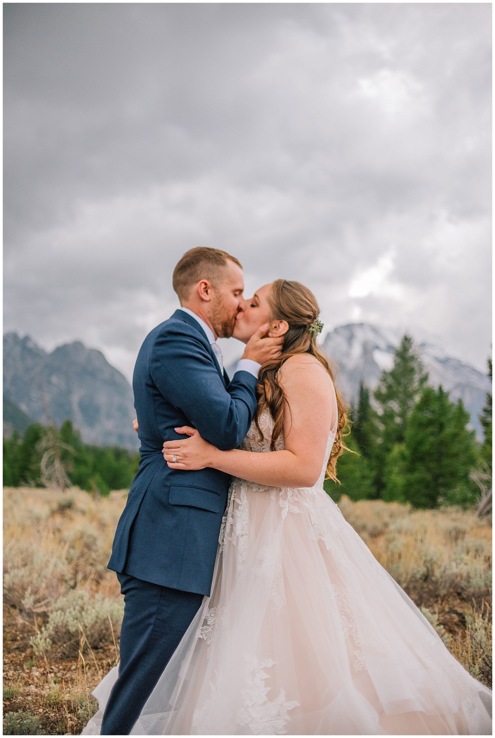 national park wedding with bride and groom kissing and holding each other in front of a mountain range on a cloudy day
