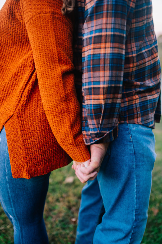 couple standing back to back while holding each others hands. Man in plaid and woman in orange sweater. Knoxville Fall photos