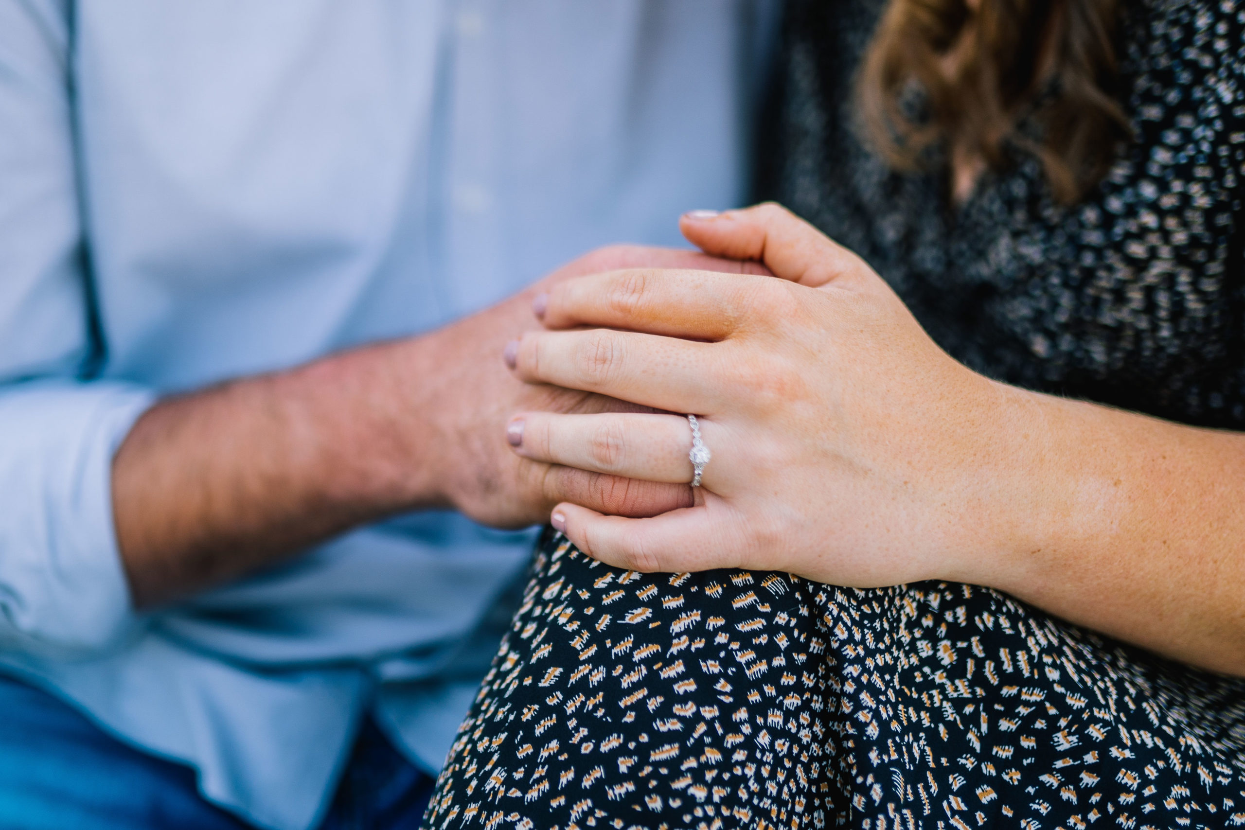 detail shot of an engagement ring in Knoxville woman wearing a block and white dress and man wearing a blue button down while holding hands
