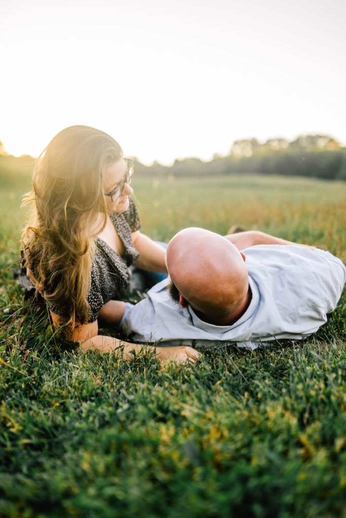 man and woman laying in a field in Knoxville Tennessee before their wedding, sunset in the background