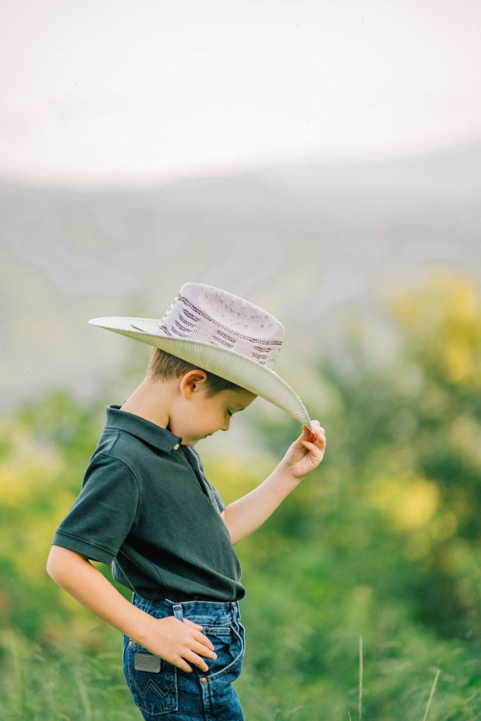 little boy in the Smokey Mountains wearing a cowboy hat and levis, he is posing with a hand on the hip and tipping his hat