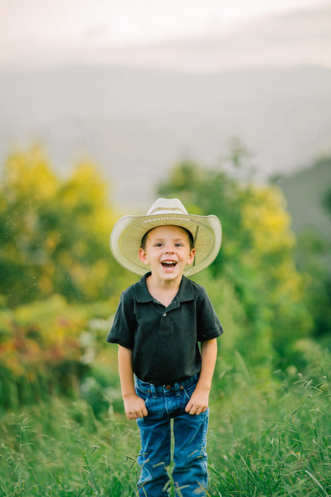 cute little boy in a cowboy hat smiling really big for the camera in th eSmokey Mountains in Tennessee