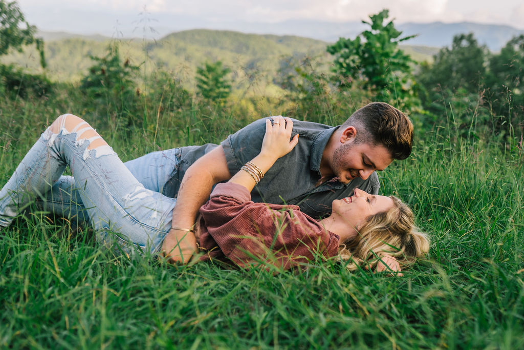man and woman lying in knoxville field during engagement session laughing and embracing