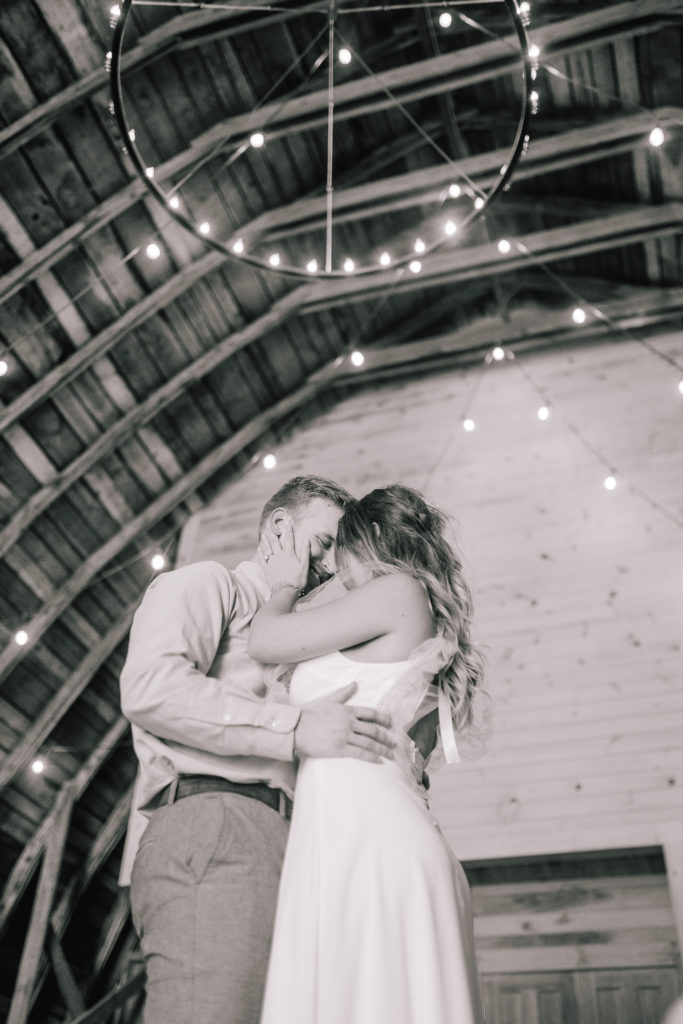 black and white photo of husband and wife embracing each other at marble gate farms under twinkle lights. 
