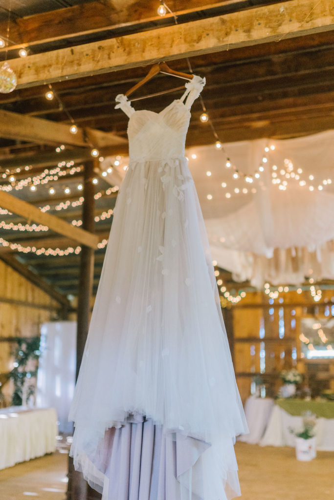 gorgeous white wedding dress hanging from a wooden ceiling surrounded by twinkle lights. wedding dress