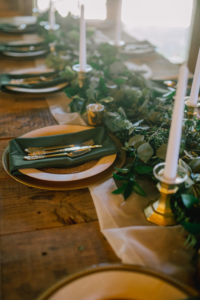 winter wedding detail shot of tableware. Dark green wedding napkins and gold candle sticks on a wood guest table