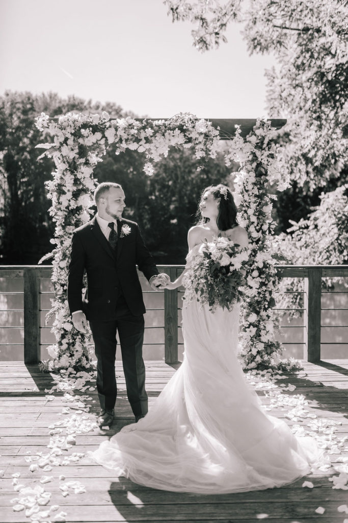 black and white photo of a bride and groom on the alter of their wedding day with white rose petals at their feet and a river in the background. Knoxville Tennessee 