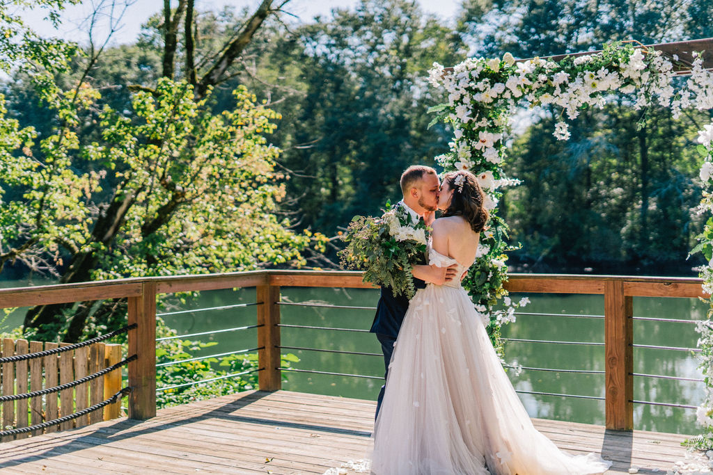 bride and groom kissing near a river in Knoxville Tennessee on a bright summer day. 