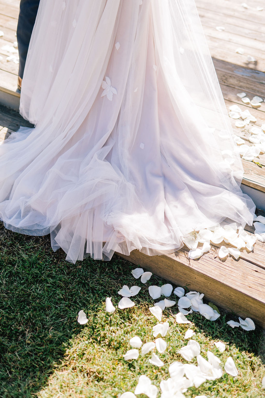 Bottom portion of a wedding dress on a set of stairs covered in white rose petals