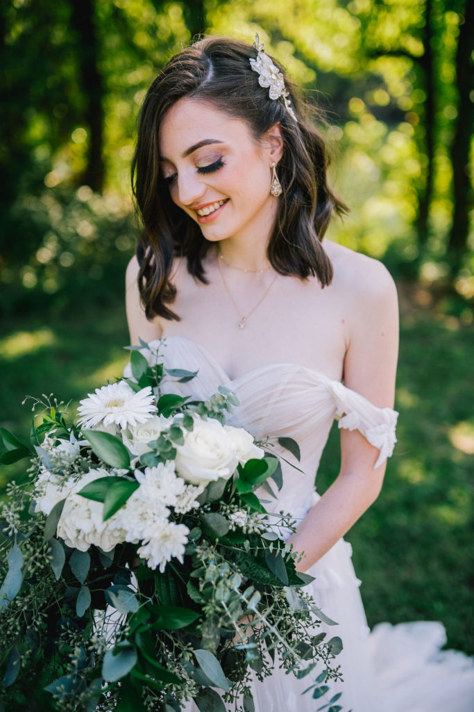 Bride smiling on her wedding day as she looks at her beautiful bouquet of white flowers and greenery
