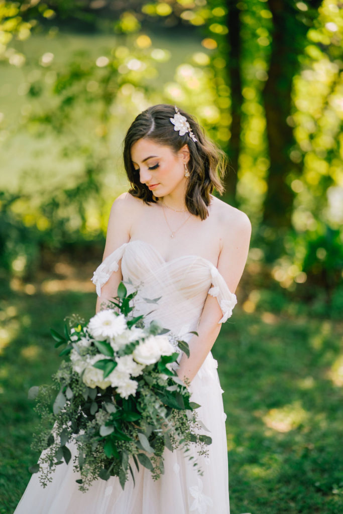 Bride looking down at her bouquet. Bride wearing an off the shoulder wedding dress with gorgeous lace flowers. In Knoxville Tennessee 