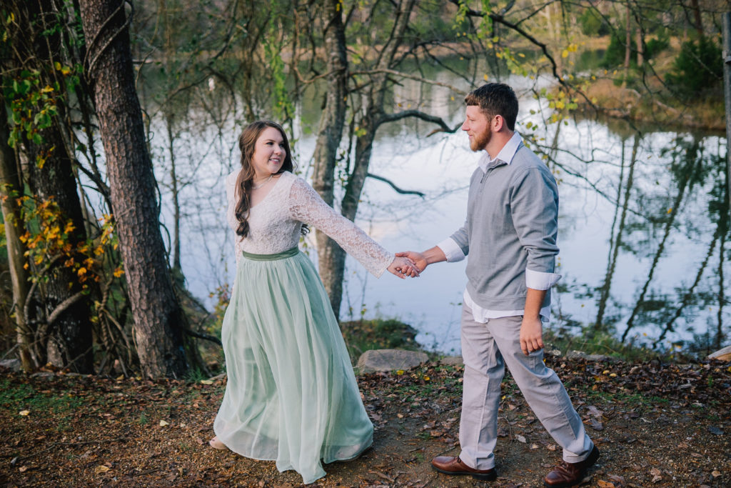 bride leading her groom as they hold hands with a lake behind them