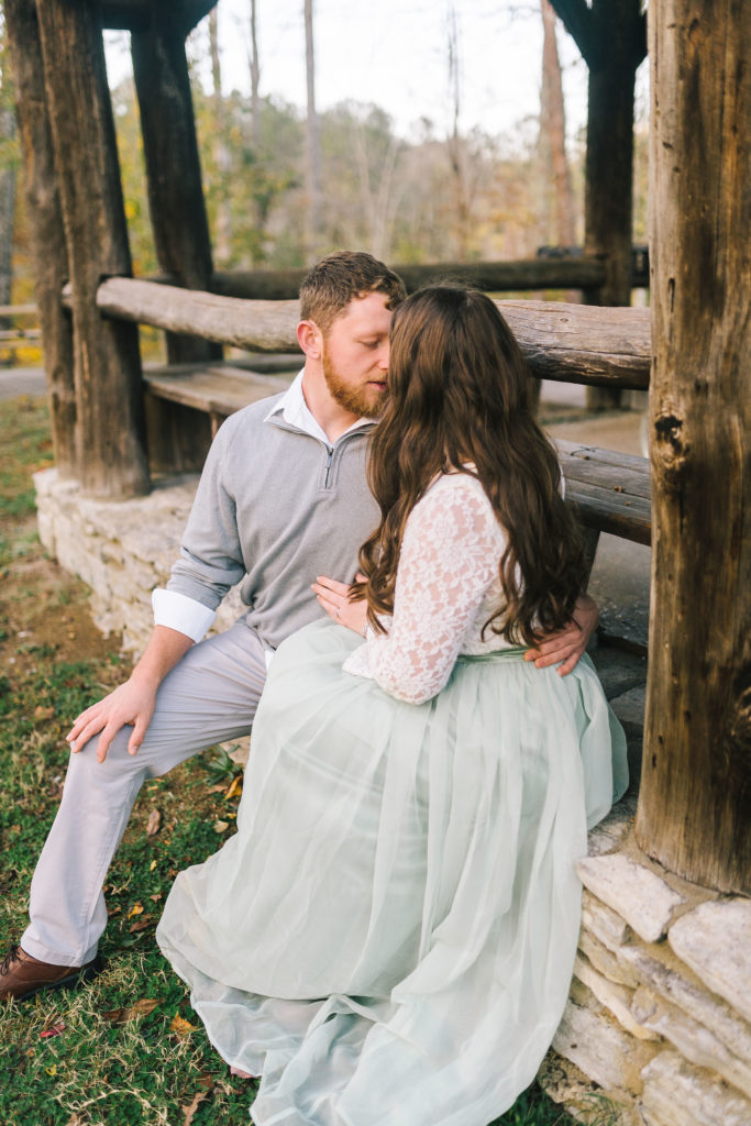 Man holding his fiancé as they sit on a front porch of an old southern cabin for an engagement session in Tennessee